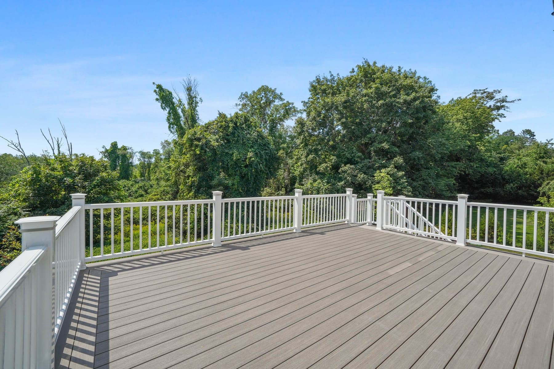 Expansive composite rear deck with white railings opening directly onto private summer woods