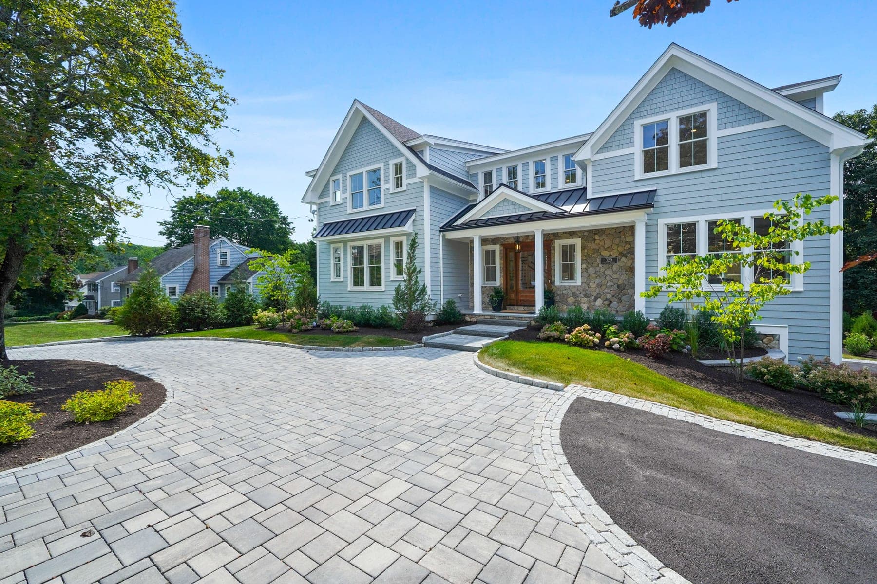 Front three-quarter view of the stone-and-shingle facade with paver motor court and hydrangeas in full summer bloom