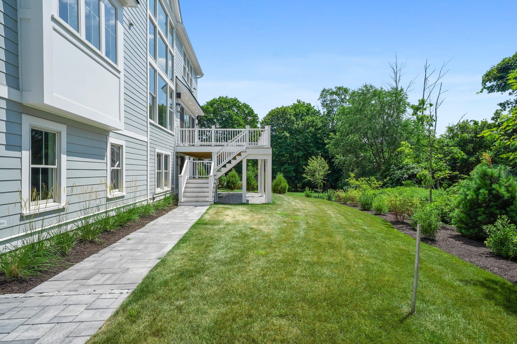 Side-yard walkway leading to the deck stairs, with manicured lawn and private wooded border