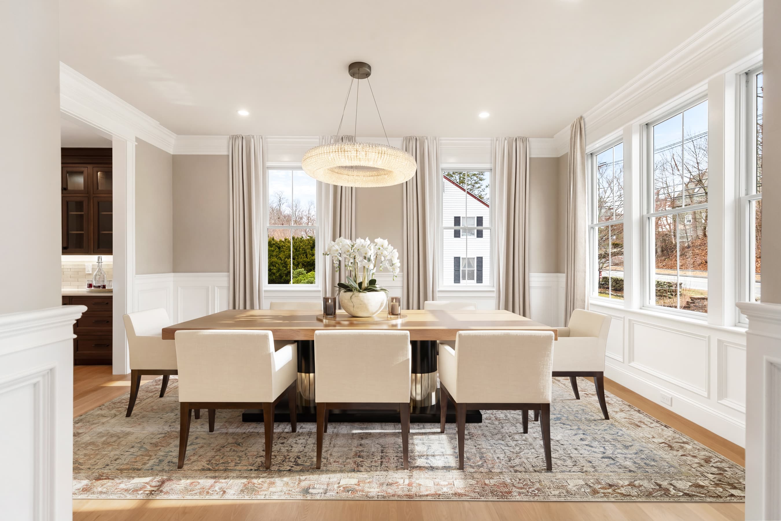 Formal dining room with round chandelier, elegant table setting, and wainscoting — virtually staged