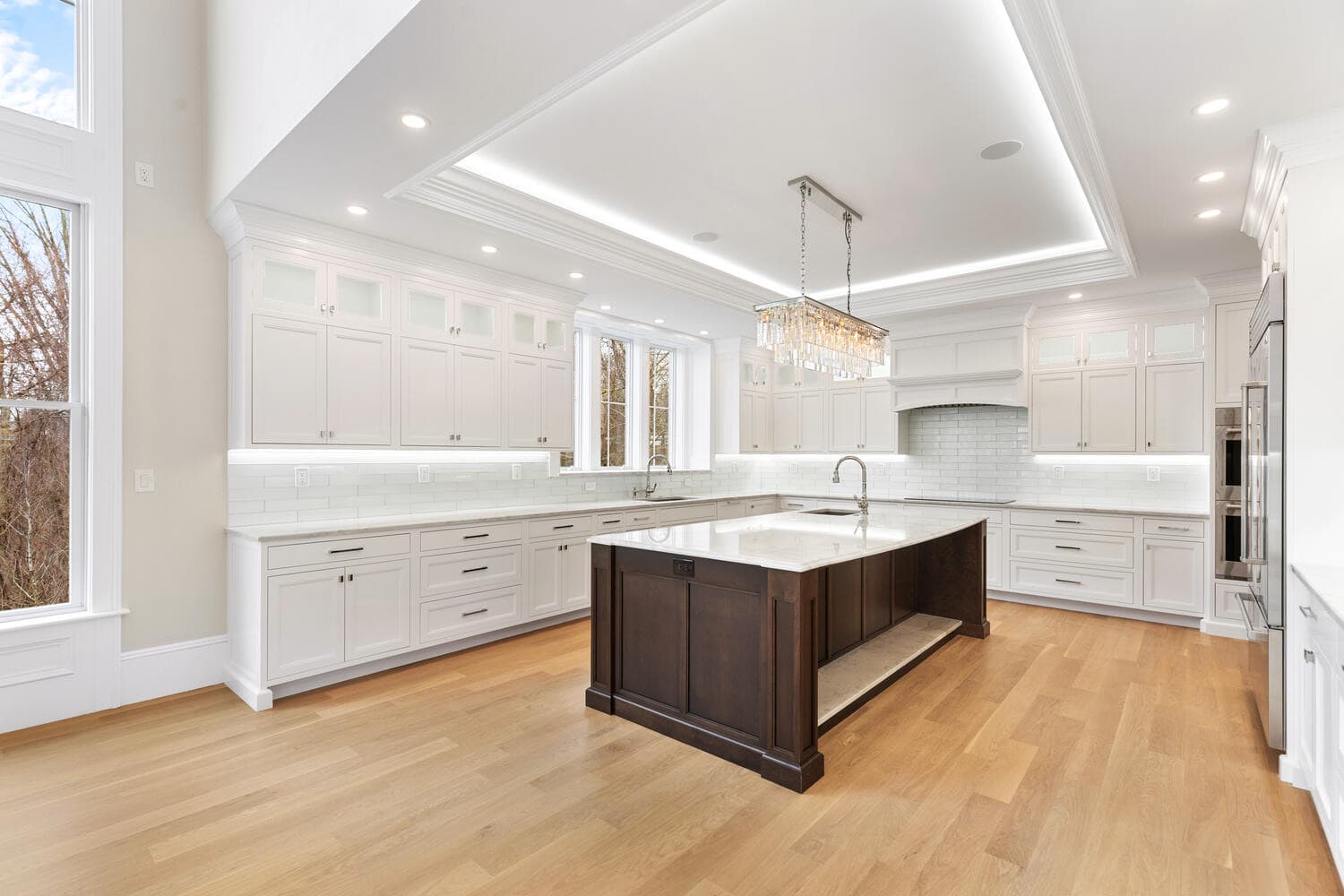 Grand kitchen with coffered ceiling, white cabinetry, dark cherry island, and crystal chandelier