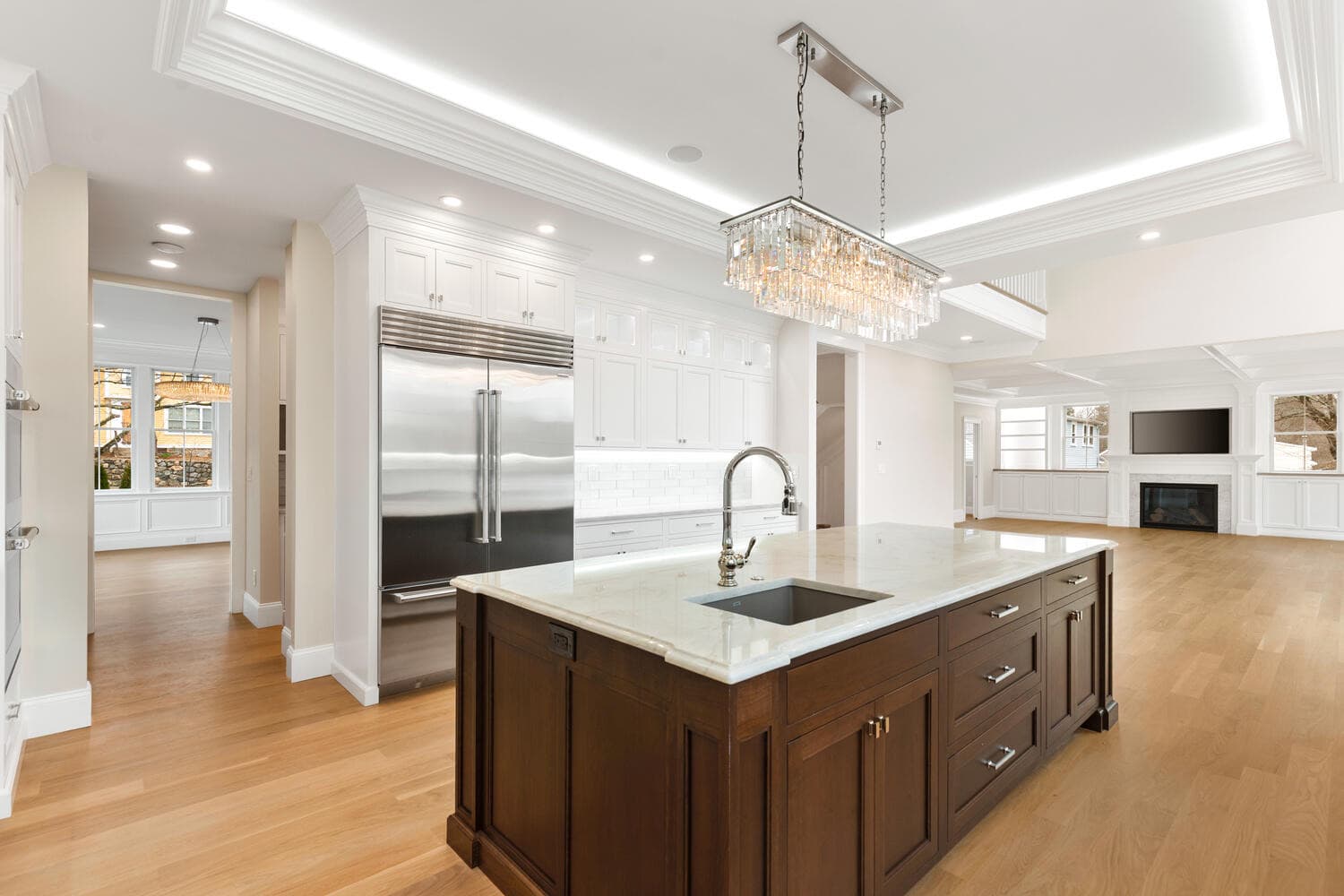 Kitchen island with dark cabinetry, marble counters, crystal linear chandelier, and stainless steel appliances