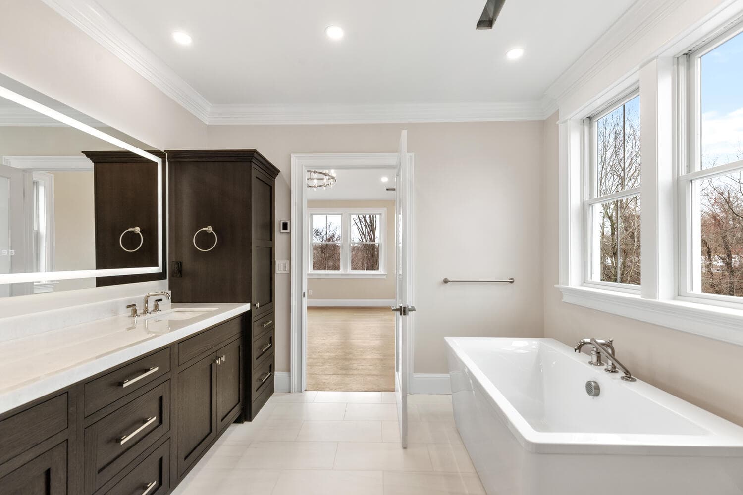Primary bathroom with dark cabinetry, marble counters, dual vanity, and soaking tub
